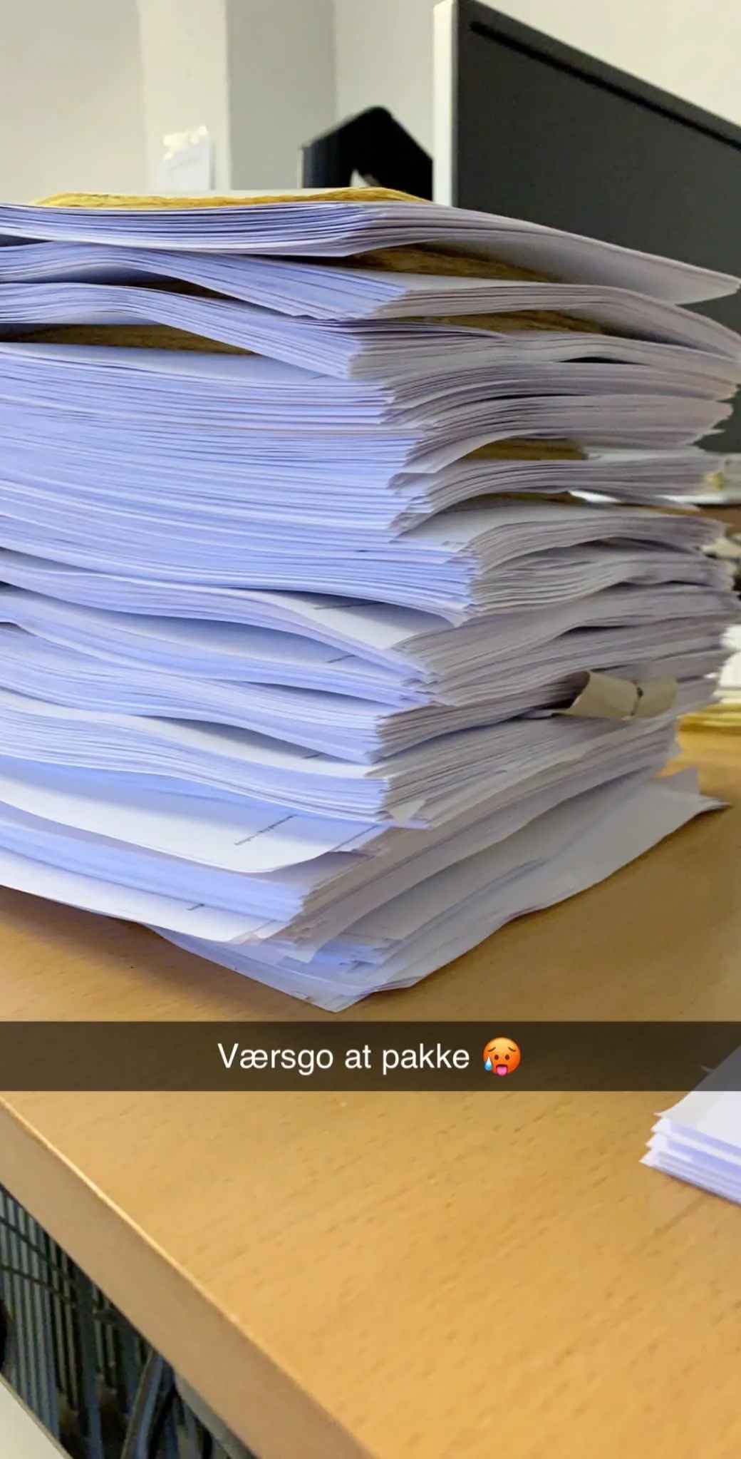 En høj stak udskrevne ordresedler på et bord med teksten “Værsgo at pakke”.